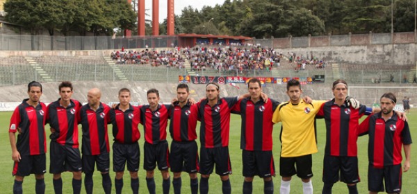 La formazione dell'Aquila. Sullo sfondo la tifoseria rossoblu