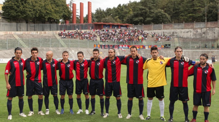 La formazione dell'Aquila. Sullo sfondo la tifoseria rossoblu